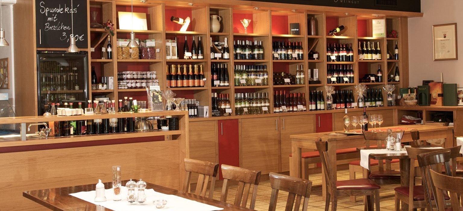 Weinrestaurant & Vinothek Kaisergarten - im Vordergrund ein eingedeckter Tisch und im Hintergrund ein Weinregal mit Weinen des Weinguts Biegler & Brand